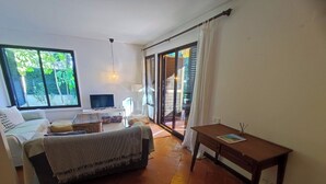 A bedroom with a bed, a TV, a desk, and a view of the outdoors through a sliding door.