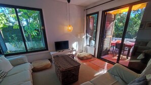 A living room with a sofa, ottoman, TV, and a view of the outdoors.
