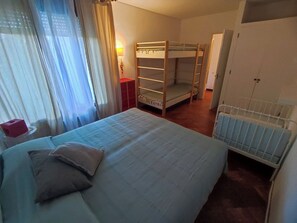 Ein Zimmer mit Etagenbetten, einem Einzelbett, einem Heizkörper und einem fenster mit Vorhängen.