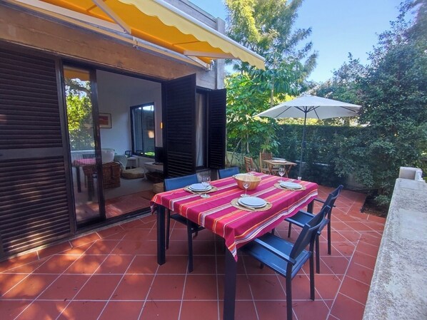Eine Terrassensitzgelegenheit im Freien mit Esstisch, überdachtem Sitzbereich und Blick ins grüne Umland.