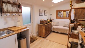 A compact kitchen with a wooden countertop, a sink, and a stove. There is a wooden cabinet with dishes and a mirror above the sofa. - Tucked Away (Evesham)