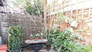 A garden with a wooden table and chairs, surrounded by potted plants and a brick wall. - Tucked Away (Evesham)