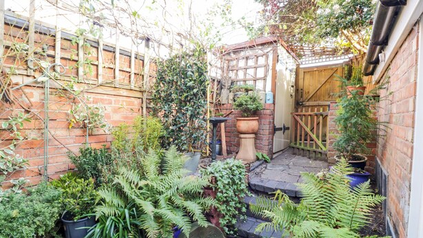 A small, enclosed garden area with various potted plants and a wooden pergola. - Tucked Away (Evesham)