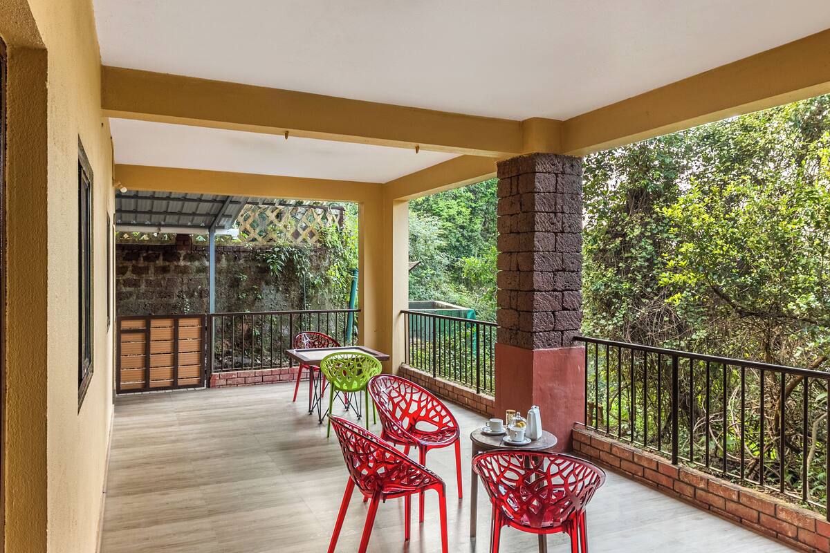 A balcony with a wooden floor, red chairs, a table, and a brick pillar.