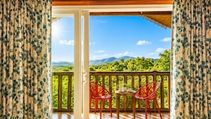 An open balcony with a wooden floor, two red chairs, and a table with a small plant. - Nature Trails Rock Valley Goa (Ponda)
