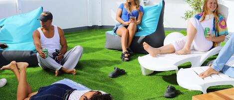 A rooftop lounge with green artificial grass, white lounge chairs, and a few people relaxing.
