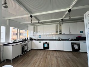 A modern kitchen with white cabinets, a built-in oven, and a large window providing natural light. - La Isleta Nest Hostel (Las Palmas de Gran Canaria)