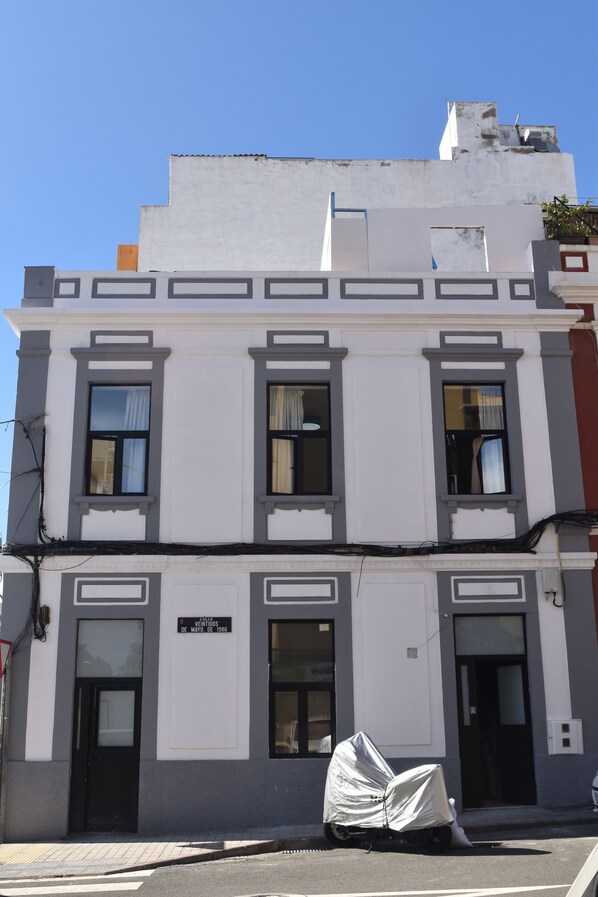 Un edificio de dos pisos con fachada blanca y detalles grises. En la planta baja se puede leer un letrero que dice "VENDIDOS DE MAYO DE 1886".