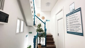 A staircase with a blue handrail, a potted plant, and a sign with check-in times. - La Isleta Nest Hostel (Las Palmas de Gran Canaria)