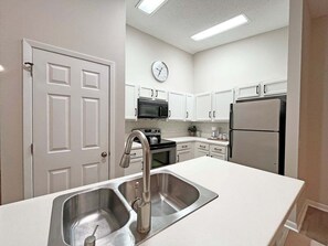 A modern kitchen with white cabinetry, stainless steel appliances, and a double sink. - Conquistador 8 Navarra Ct (St. Augustine)