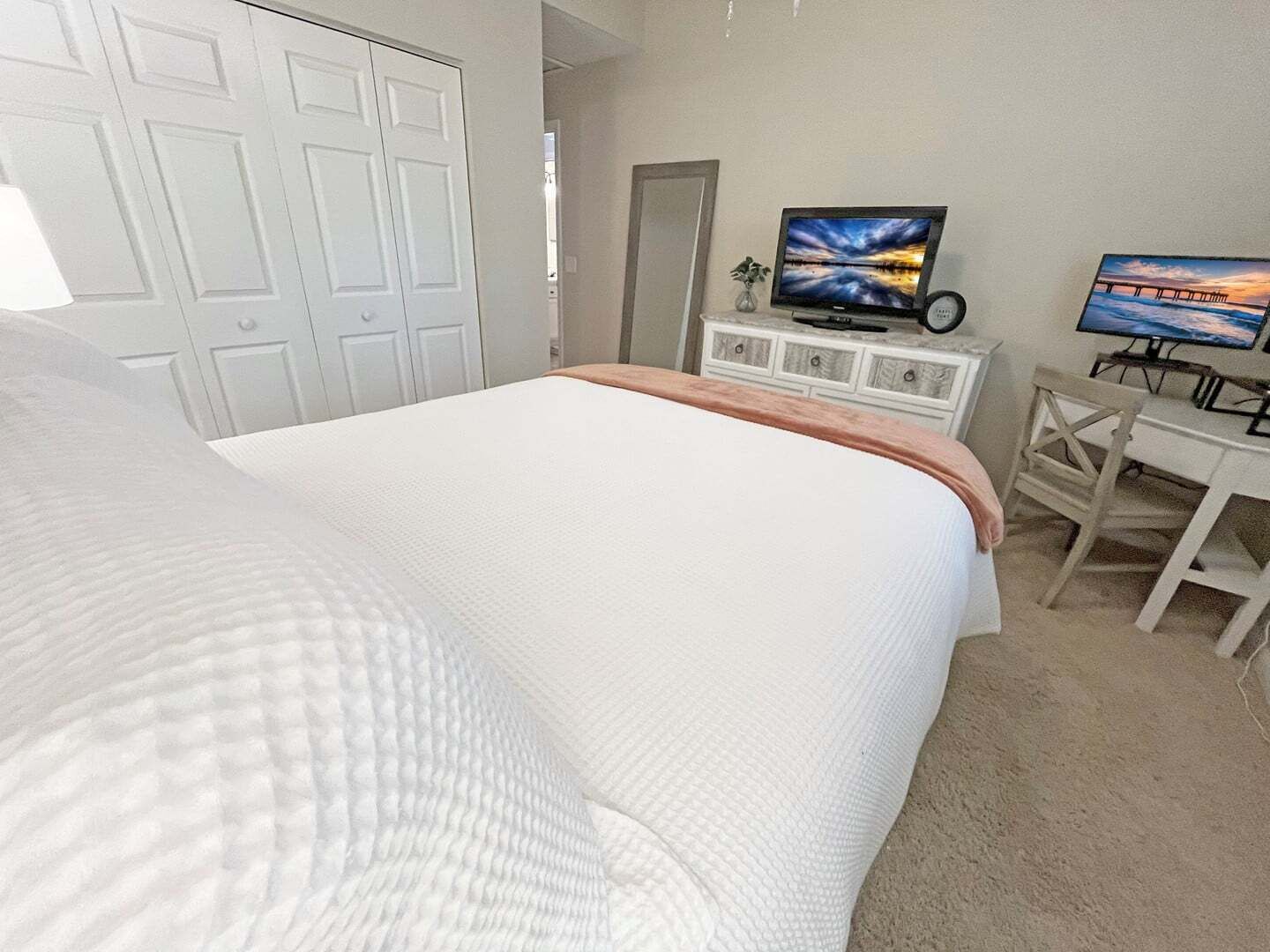 A bedroom with a large bed, a desk with a computer, and two TVs on the wall.