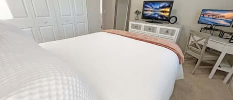 A bedroom with a large bed, a desk with a computer, and two TVs on the wall.