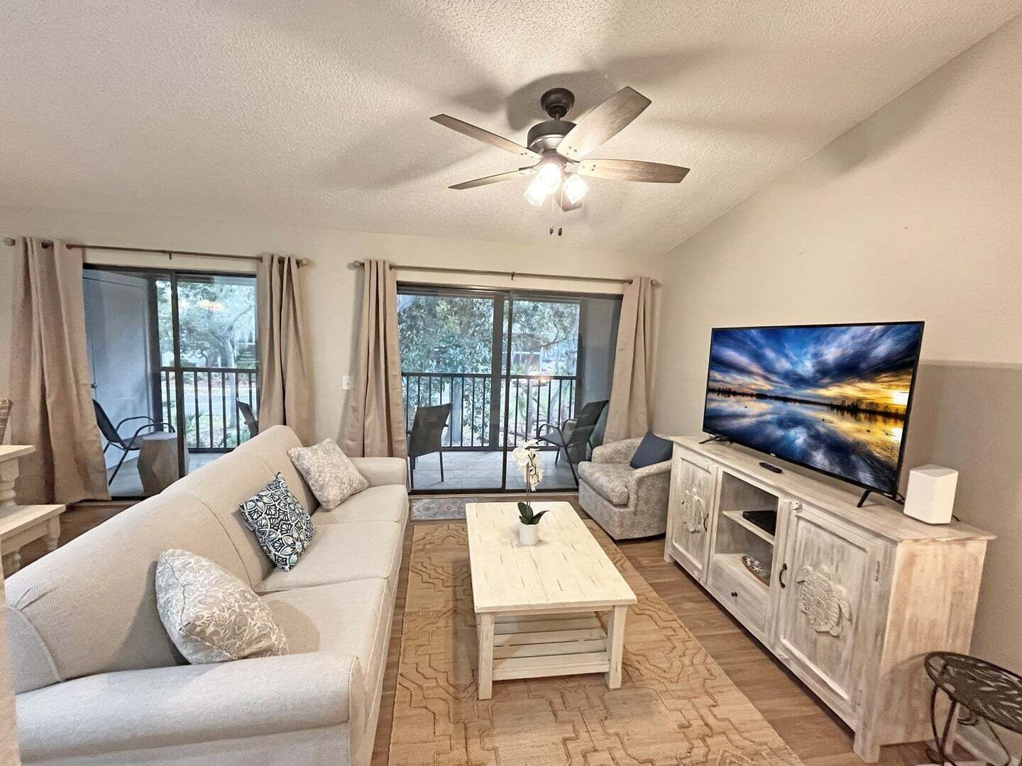 A living room with a sofa, coffee table, TV, and a ceiling fan.