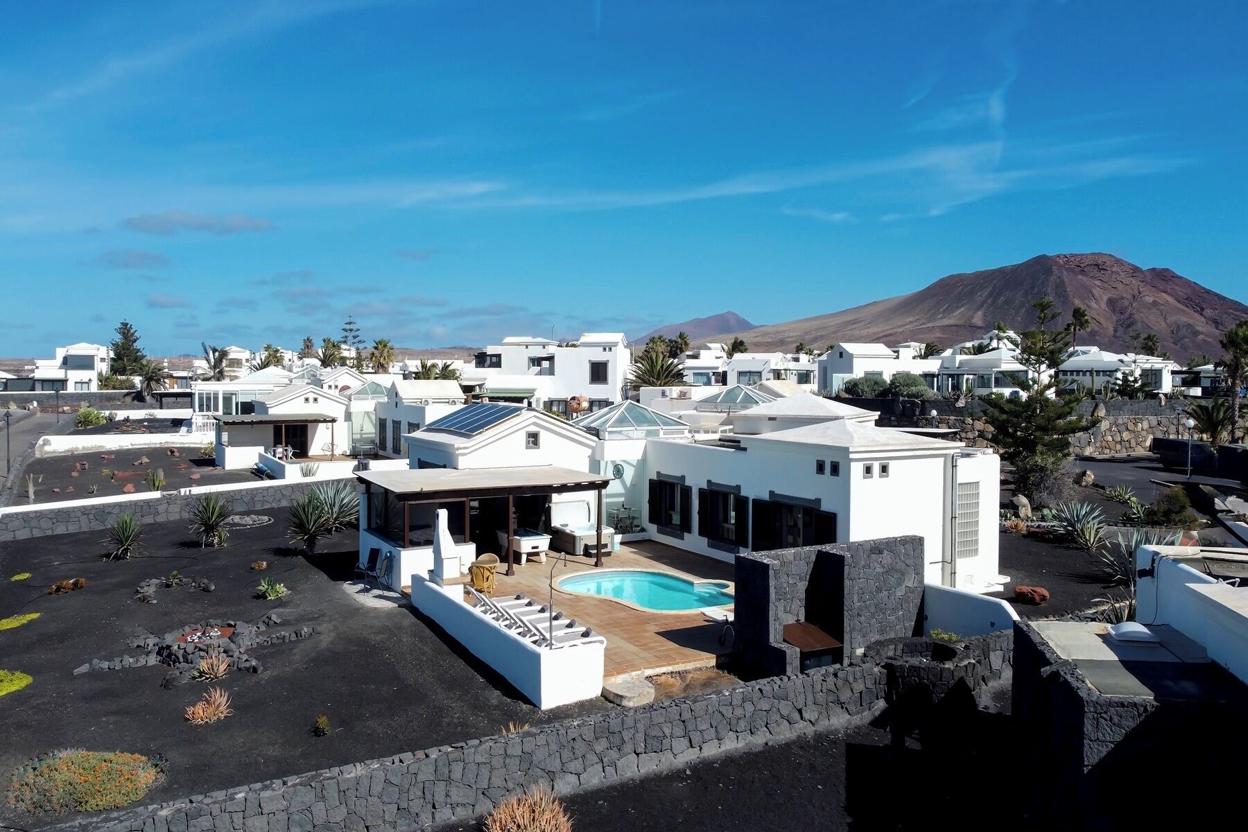 A modern resort with white buildings, a swimming pool, and a mountain in the background.