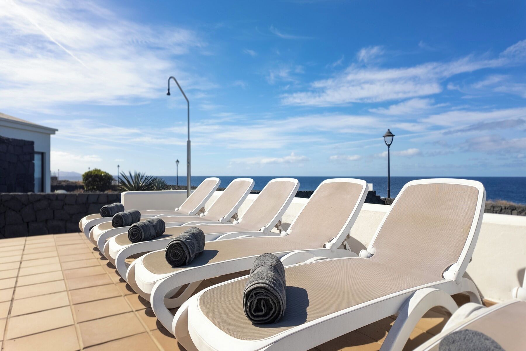 A row of sun loungers with towels, a stone wall, and a view of the ocean.
