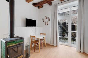 A room with a wood-burning stove, a TV mounted on the wall, a table with chairs, and a large window with curtains. - Apartment Altes Forstamt – Stilvolles Wohnen im historischen Gebäude (Gernsbach)