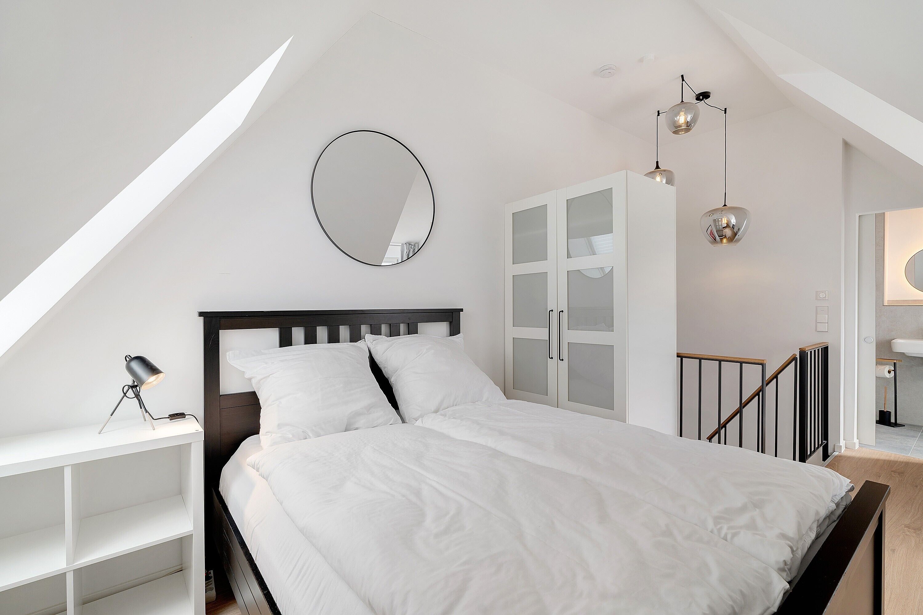 A bedroom with a bed, a bedside table, a wardrobe, and a staircase.