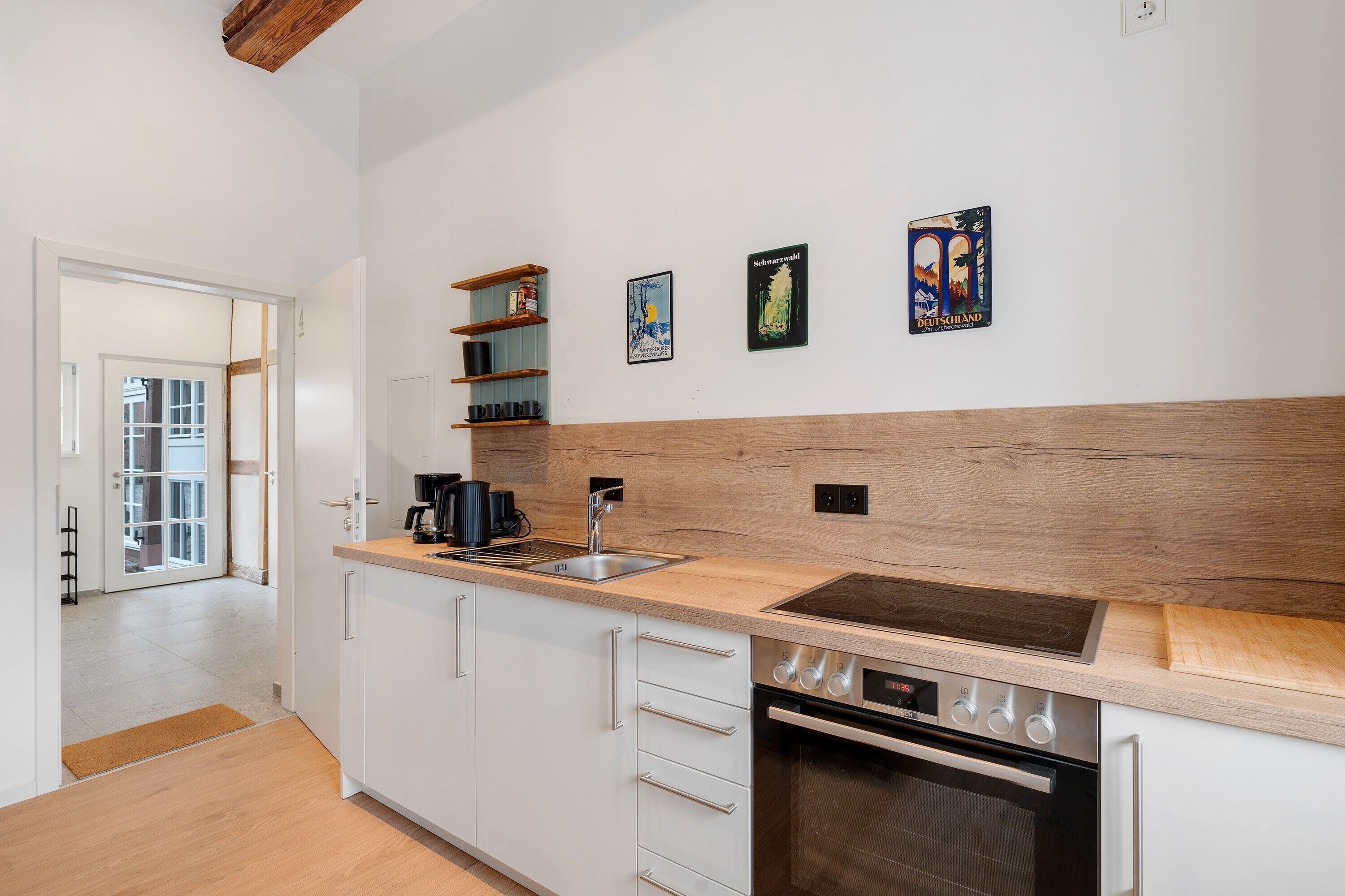 Una cocina moderna con armarios blancos, encimera de madera, horno empotrado y cafetera.
