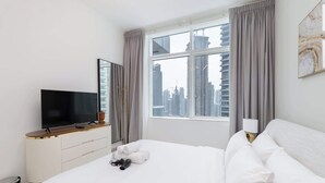 Habitación de hotel con cama, televisor sobre una consola de madera, ventana con cortinas y vista a la ciudad.