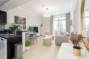 A modern apartment with a kitchen, dining area, and living room. It features a large window, a flat-screen TV, and a sofa. - StayShort - Refined 1 Bedroom Retreat Sleeps 4 in Dubai Marina (Dubai Marina)