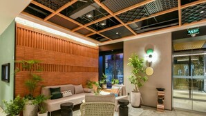 Un hall d’entrée moderne avec un mur à lattes de bois, un espace salon comprenant un canapé et des fauteuils, des plantes en pot et une grande fenêtre offrant une vue dégagée.
