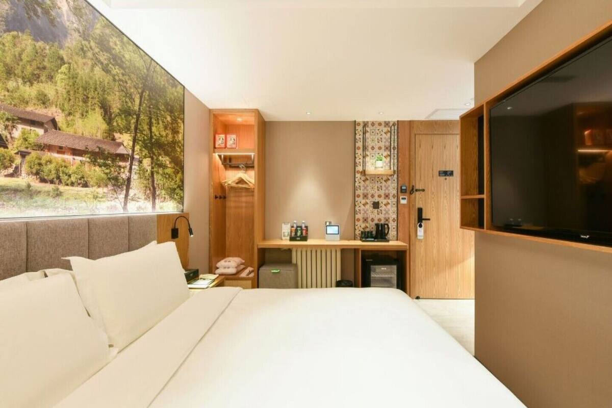 Una habitación de hotel moderna con una cama grande, televisión, escritorio con computadora y vista a un paisaje montañoso.