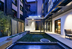 Un hôtel moderne avec une façade attrayante, une entrée bien éclairée, un petit jardin et une piscine.