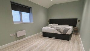 Quarto com cama, janela, radiador e piso de madeira.
