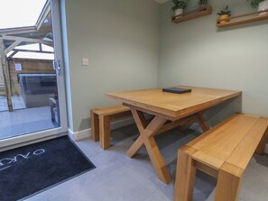 A wooden dining table with benches in a room with a glass door leading outside. - Oak Barn (Chester)