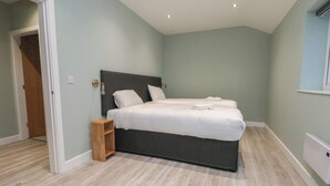 A bedroom with a large bed, a wooden nightstand, and a light-colored wooden floor. - Oak Barn (Chester)