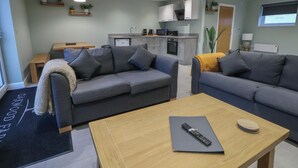 A modern living room with two grey sofas, a wooden coffee table, and a kitchen area in the background. - Oak Barn (Chester)