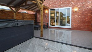 A patio area with a wooden pergola, a covered seating area, and a sliding glass door leading to a kitchen. - Oak Barn (Chester)