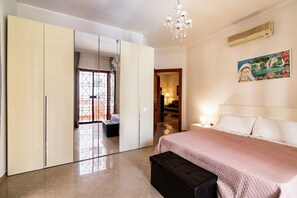 Ein Schlafzimmer mit einem Bett, einem Kleiderschrank, einer Bank, einer Chandelüster und einem Gemälde an der Wand.
