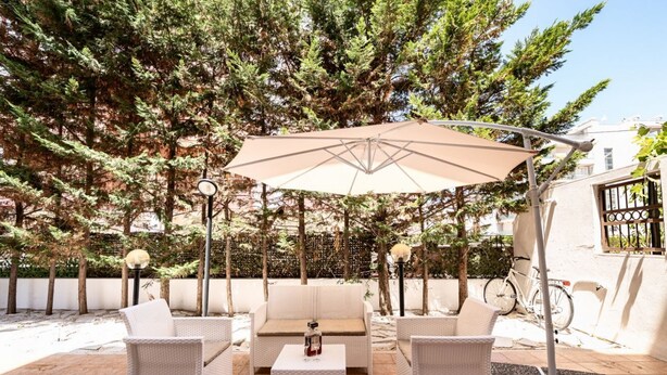 An outdoor seating area with wicker furniture, a large umbrella, and a bicycle in the background. - GuestHost - The House of Pines (Trani)