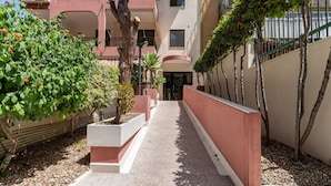 A pathway leading to a building with a red and white facade, surrounded by greenery and trees. - GuestHost - The House of Pines (Trani)