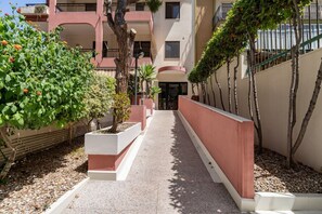 Ein Weg führt zu einem Gebäude mit roter und weißer Fassade, umgeben von Grünpflanzen und Bäumen.