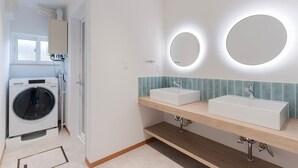 Een moderne badkamer met twee wastafels, een wasmachine en een spiegel met ingebouwde verlichting.
