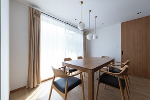 Ein moderner Essbereich mit Holztisch und Stühlen, großen Fenstern mit Vorhängen und Pendelleuchten.