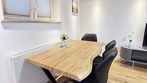 Een moderne eetruimte met een houten tafel en zwarte stoelen, een radiator en een raam met jaloezieën.