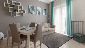 A modern living room with a dining table, chairs, a sofa, a wall-mounted shelf with plants, and artwork. - GuestHost - M1 Gambara Balcony Studio (Milano)