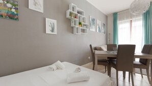 A modern hotel room with a bed, a dining table, chairs, and wall-mounted shelves with plants. - GuestHost - M1 Gambara Balcony Studio (Milano)