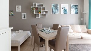 A modern living room with a dining table, sofa, and a white shelving unit with plants. - GuestHost - M1 Gambara Balcony Studio (Milano)