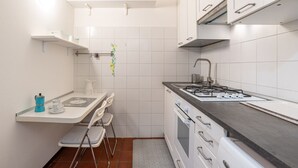 Eine kompakte Küche mit weißen Schränken, einem Gasherd, einer Spüle und einer kleinen Essecke mit Stuhl und Tisch.