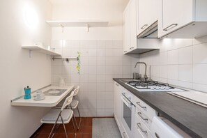 A compact kitchen with white cabinets, a gas stove, a sink, and a small dining area with a chair and table. - GuestHost - Nice studio apartment located on the ground floor of a residential building with a shared garden (where you can park bicycles).Please note: it is not possible to park just outside the house. The closest parking (not guaranteed) is located in  (Como)
