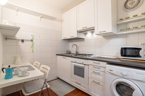 A kitchen with white cabinets, a gas stove, a microwave, and a washing machine. - GuestHost - Nice studio apartment located on the ground floor of a residential building with a shared garden (where you can park bicycles).Please note: it is not possible to park just outside the house. The closest parking (not guaranteed) is located in  (Como)