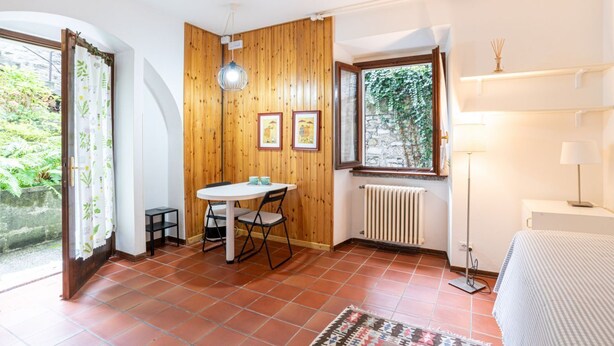 Ein Zimmer mit Holzwand, einem Fenster mit Blick auf Grünflächen, einem Tisch mit Stühlen, einem Heizkörper und einem Bett.