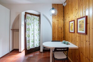 A dining area with a white table, black chairs, a hanging light fixture, and wooden paneling on the walls. - GuestHost - Nice studio apartment located on the ground floor of a residential building with a shared garden (where you can park bicycles).Please note: it is not possible to park just outside the house. The closest parking (not guaranteed) is located in  (Como)