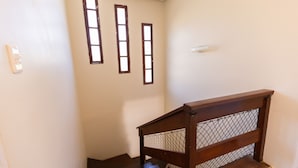 Eine Treppe mit Holzgeländer und einer Metall-Sicherheitsbarriere. In der Wand befinden sich drei Fenster mit Holzrahmen.