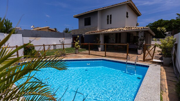 Ein Schwimmbad mit gefliestem Deck, umgeben von einem eingezäunten Garten mit Kübelpflanzen.