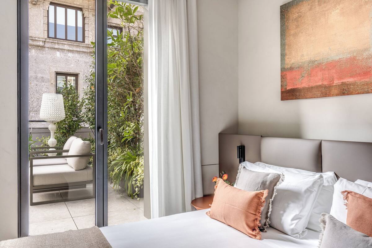 A modern bedroom with a large bed, a view of a balcony, and a painting on the wall.
